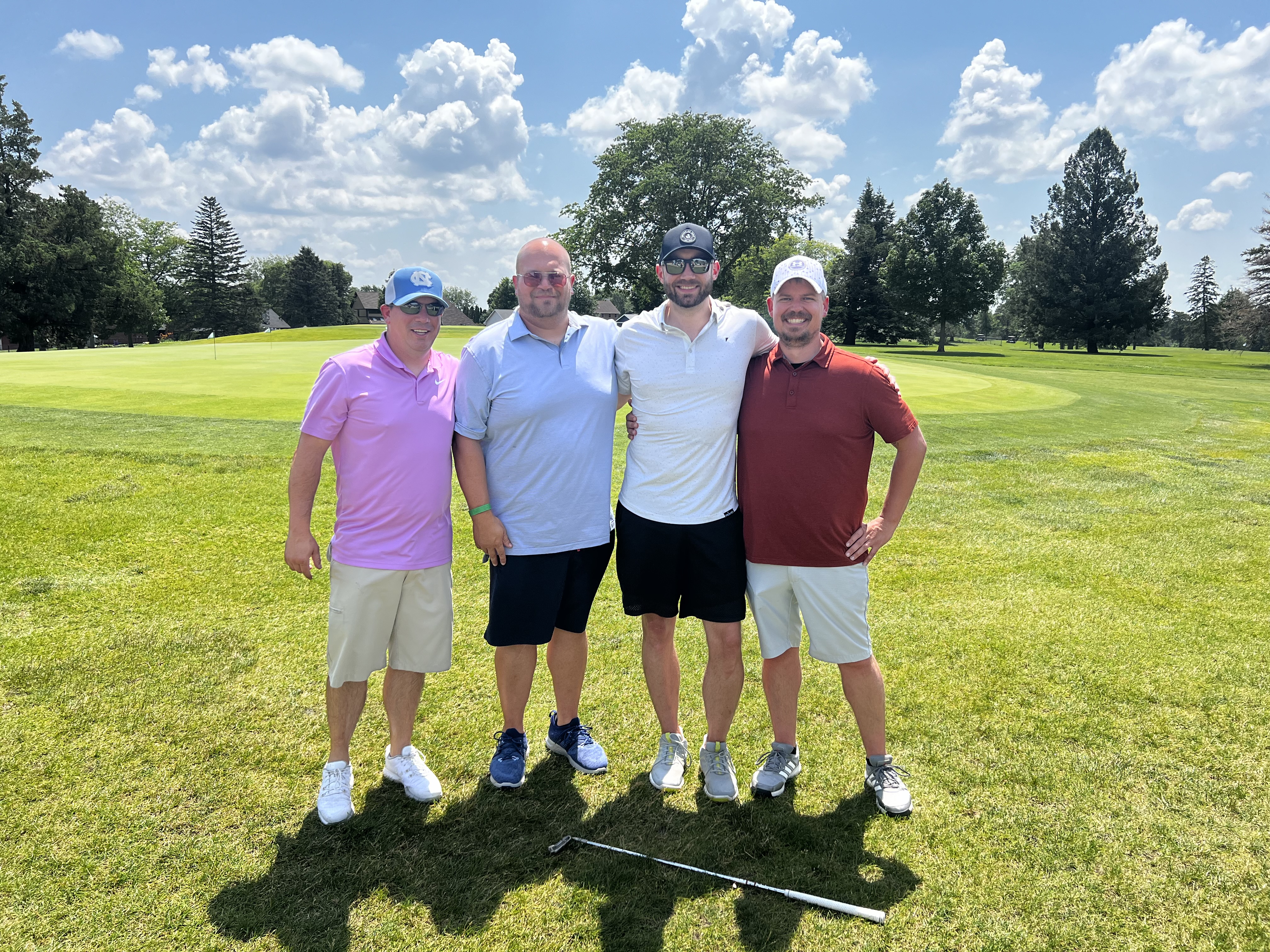 Aronson Team Photo Standing in Front of Golf Course with Trees and Cloudy Sky
